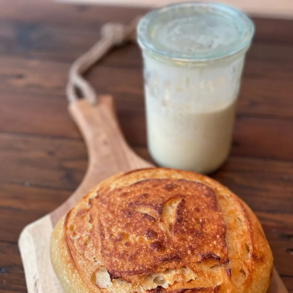 Frasco con masa madre activa junto a un pan redondo